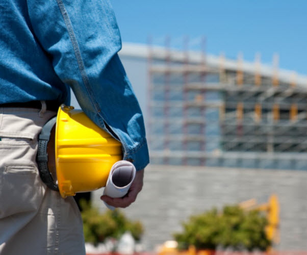 Man holding a floor plan and a hard hat facing the construction site