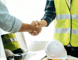 Construction worker team hands shaking after plan project contract on workplace desk